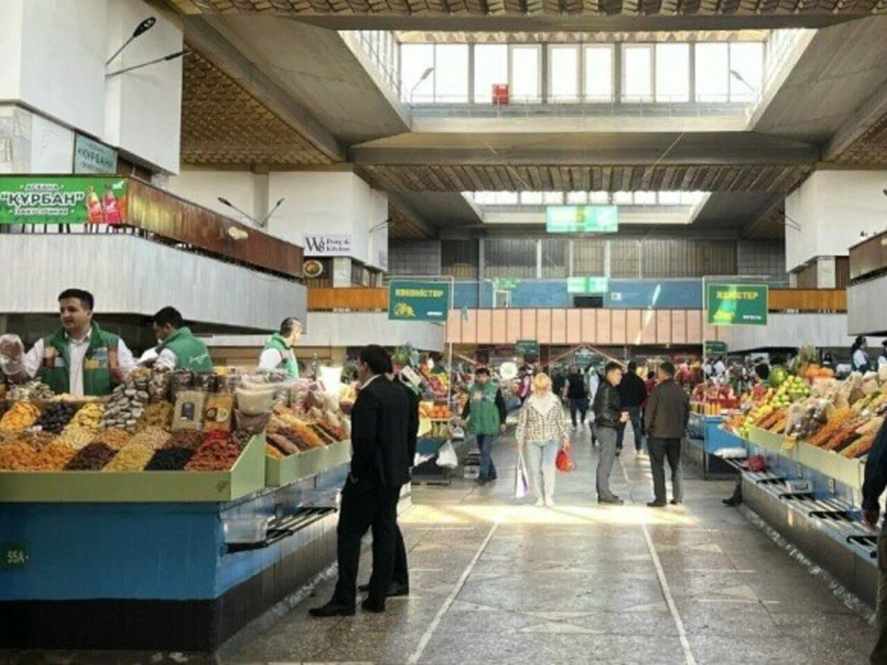 Market vendors selling dried fruits, nuts, and produce inside Green Bazaar Almaty.